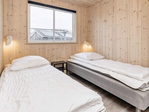 A room with two beds, wooden walls, a window, and a view of a building outside.