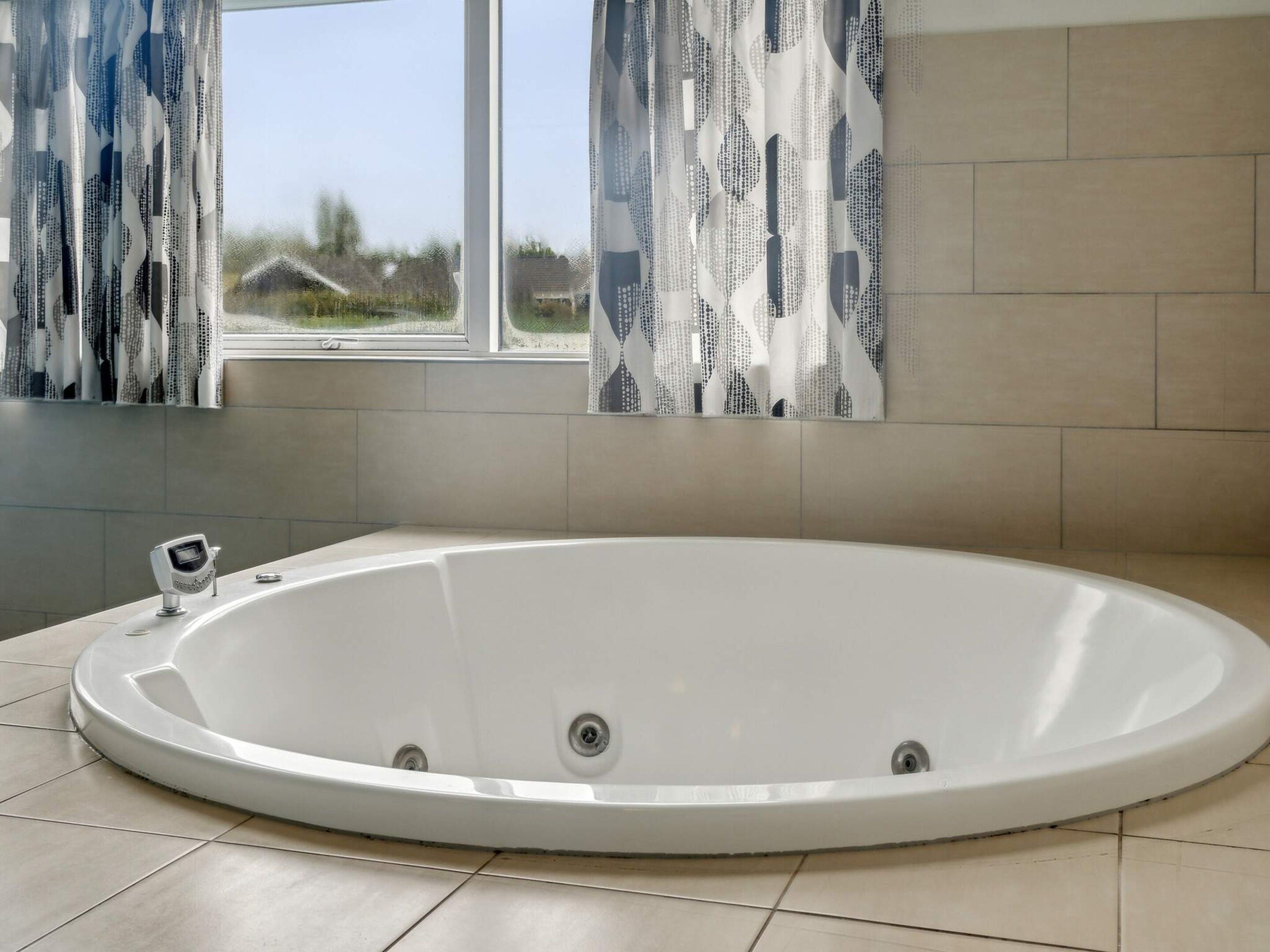 Une salle de bain moderne avec une baignoire sur pieds, une fenêtre agrémentée de rideaux à motifs et un sol carrelé.