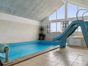 An indoor swimming pool with a slide, a window with curtains, and a potted plant.