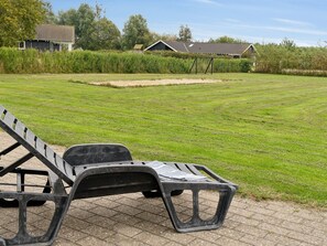 A grassy outdoor area with a single black plastic chair and a paved walkway.