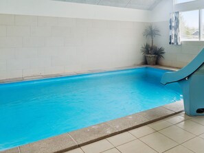 An indoor swimming pool with a clear blue water, tiled walls, and a slide.