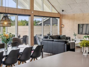 A modern living space with a large sofa, dining table, and chairs, wooden panel walls, and a television.