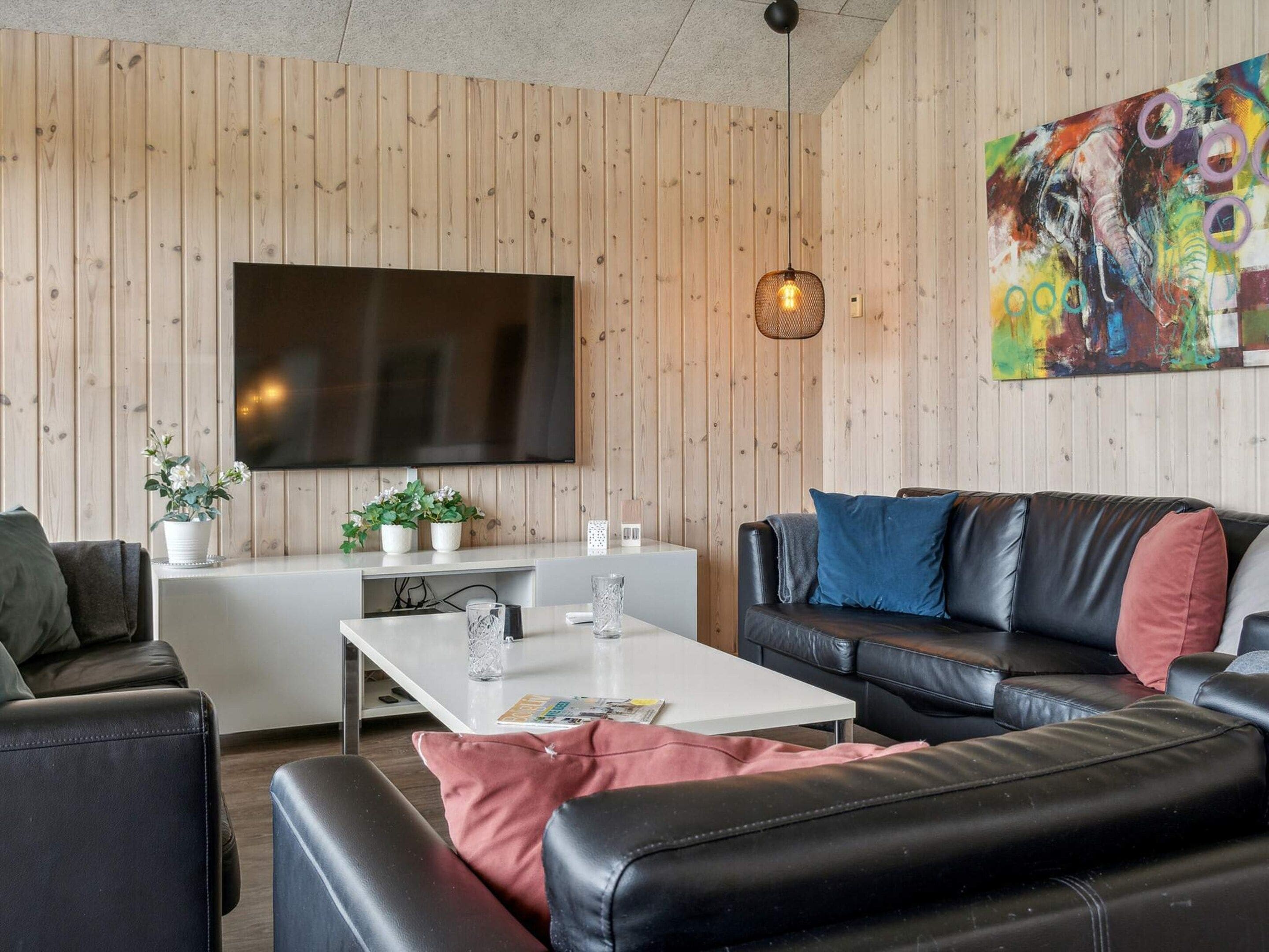 Ein modernes Wohnzimmer mit Flachbildfernseher, Ledersofa, weißem Couchtisch und Wandverkleidung aus Holz.