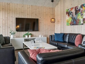Ein modernes Wohnzimmer mit Flachbildfernseher, Ledersofa, weißem Couchtisch und Wandverkleidung aus Holz.