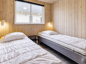 A room with two single beds, wooden walls, a window, and wall-mounted lights.