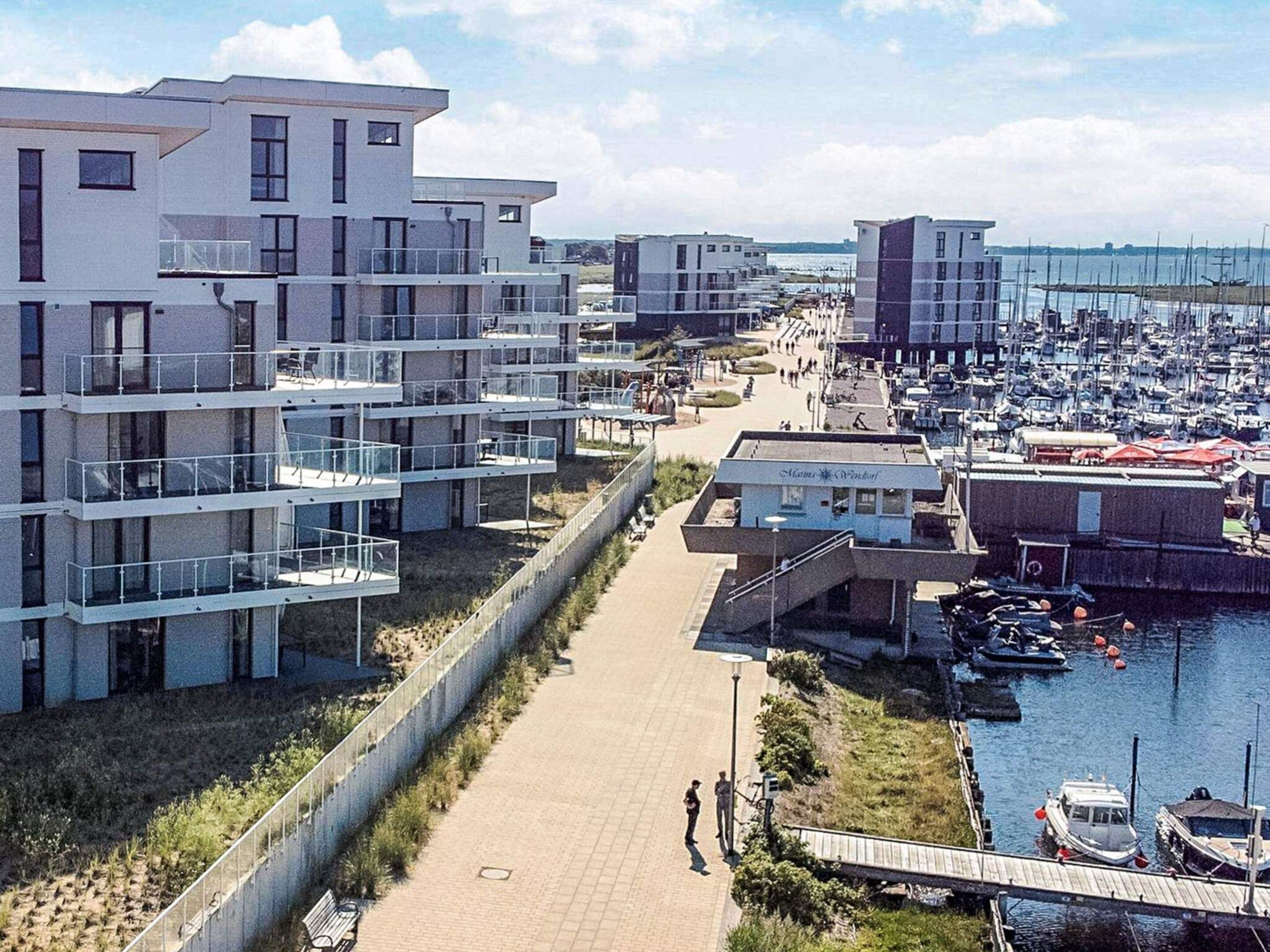 Un quartier résidentiel situé sur la côte, avec des immeubles modernes, un port de plaisance et une promenade piétonne.
