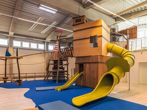 Un'area giochi al coperto con uno scivolo, strutture per arrampicata e un ponte sospeso.