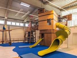 Zona de juegos interior con tobogán, estructuras para escalar y puente colgante.