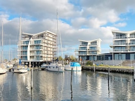 Un puerto deportivo con edificios modernos, barcos amarrados y cielo despejado.