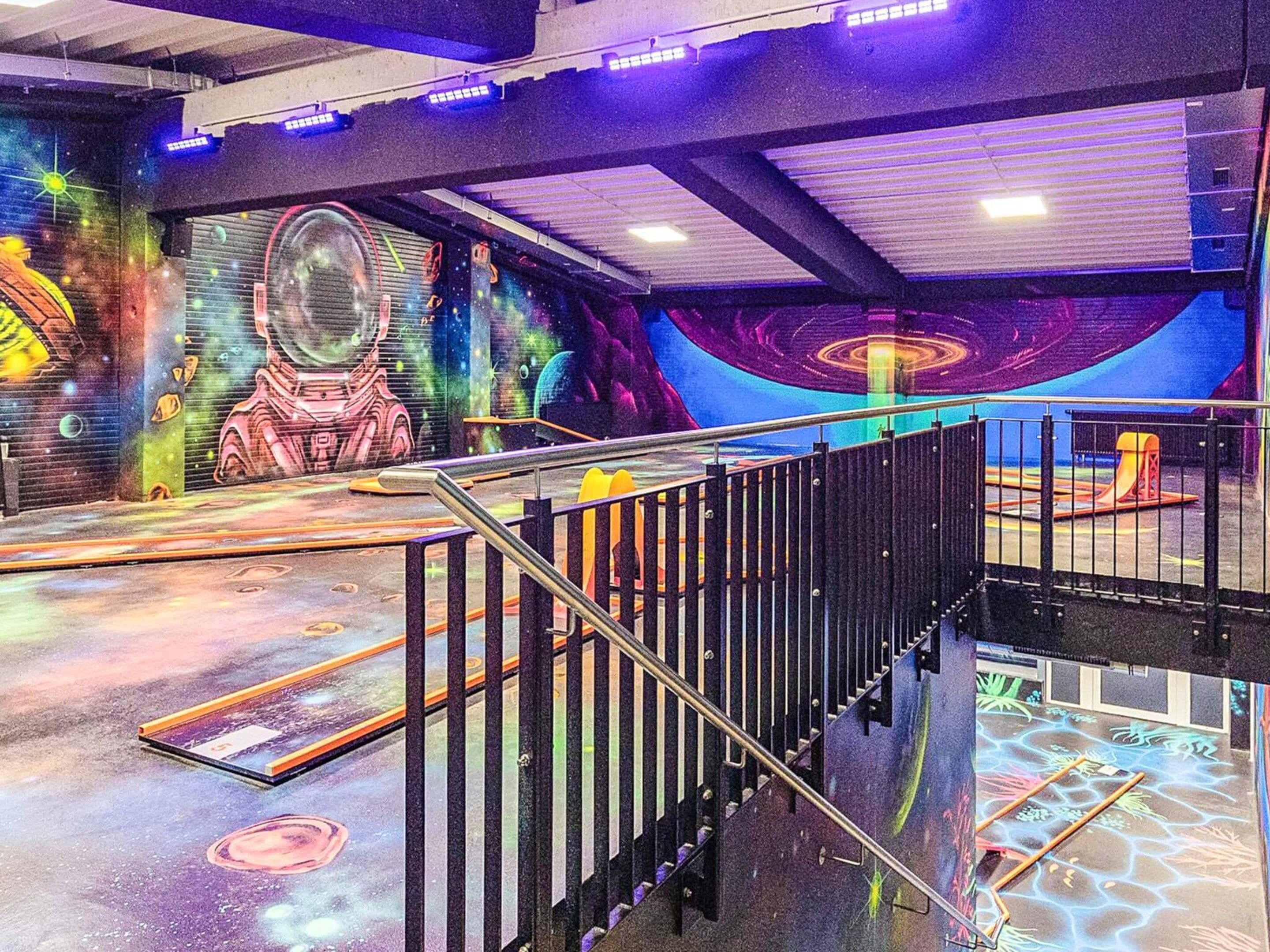 Et flerplansindretning med trappe, muralmaleri med rumtema og et legeområde med farverig gulvbelægning.