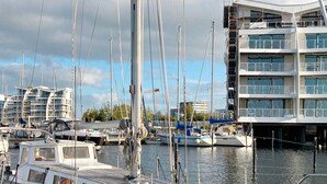 A marina with multiple boats docked, a modern building with balconies, and a cloudy sky. - Holiday Home in Wendtorf (Wendtorf)
