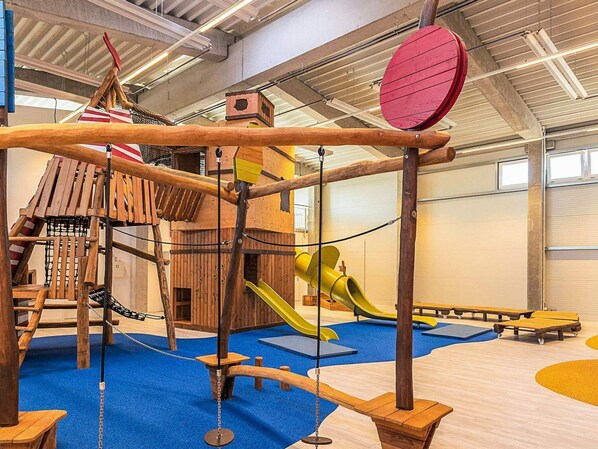 A children's play area with a wooden climbing structure, slides, and soft play mats. - Holiday Home in Wendtorf (Wendtorf)