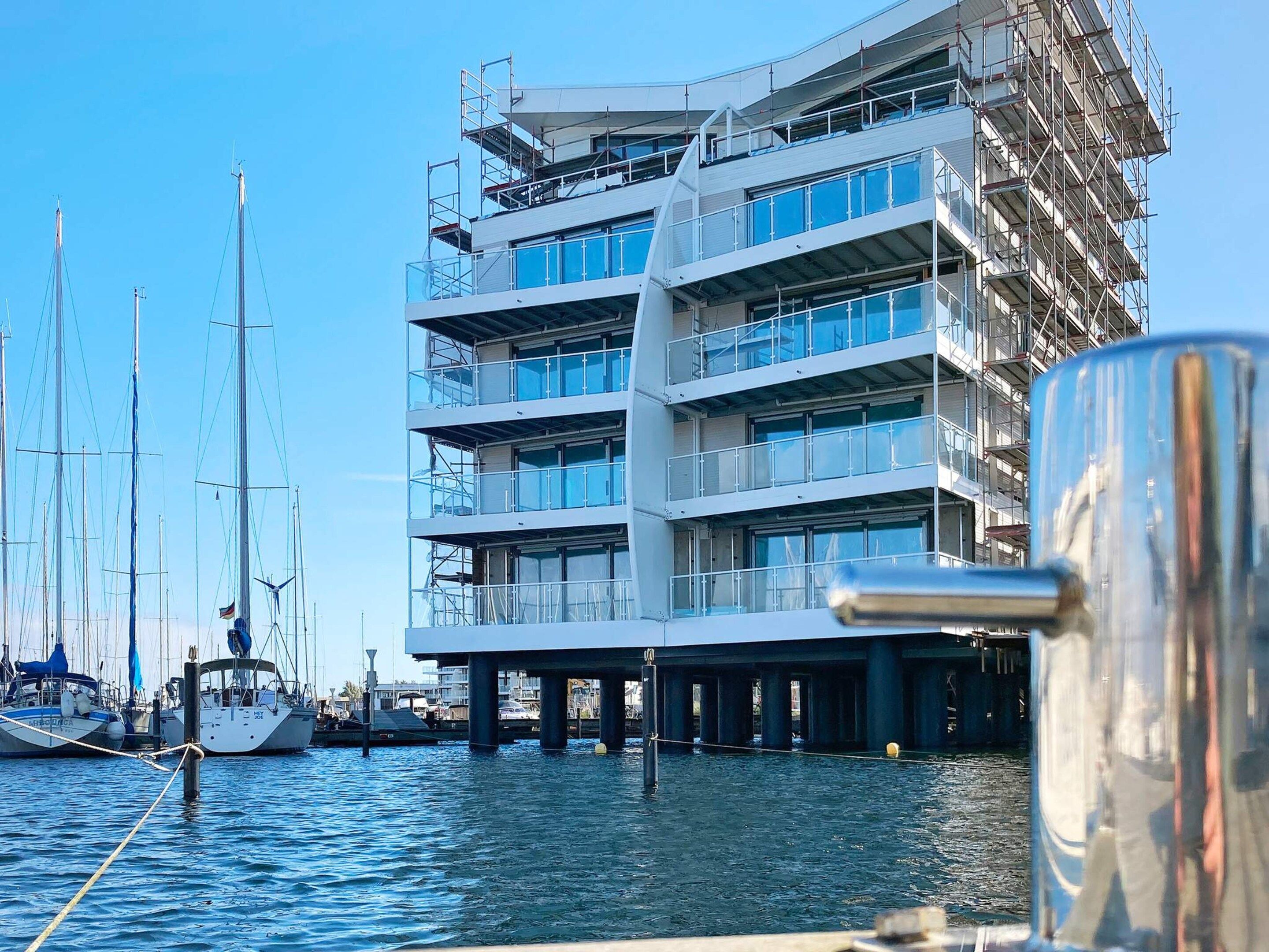 A multi-story building with balconies, a marina with boats, and a clear sky.