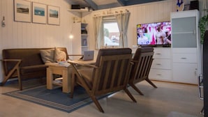 A living room with a wooden sofa, two wooden chairs, a coffee table, and a TV. - Holiday House Solvej (Brodersby)