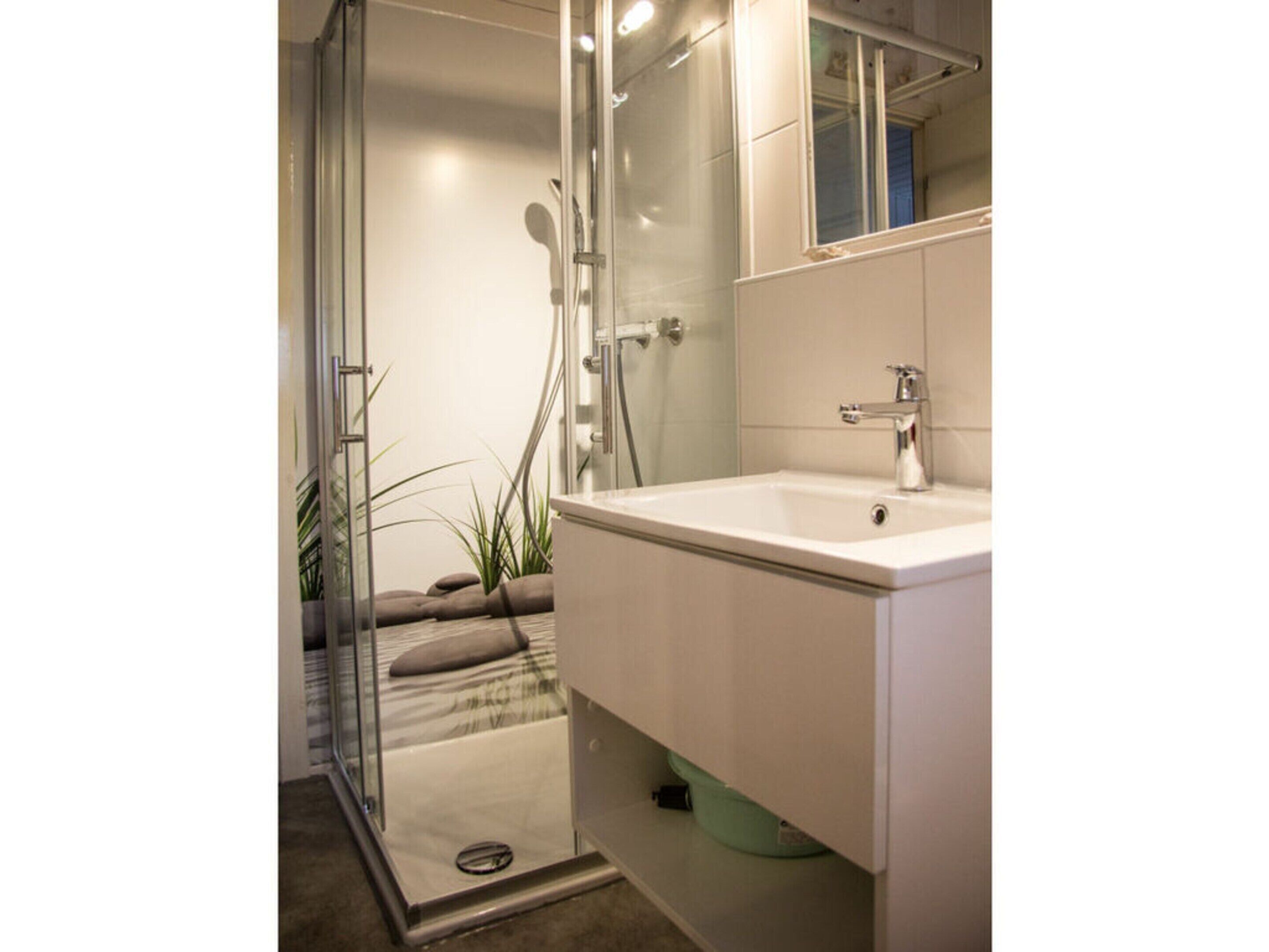 Une salle de bain moderne avec une douche à l’italienne en verre, un lavabo blanc et un miroir au-dessus du lavabo.