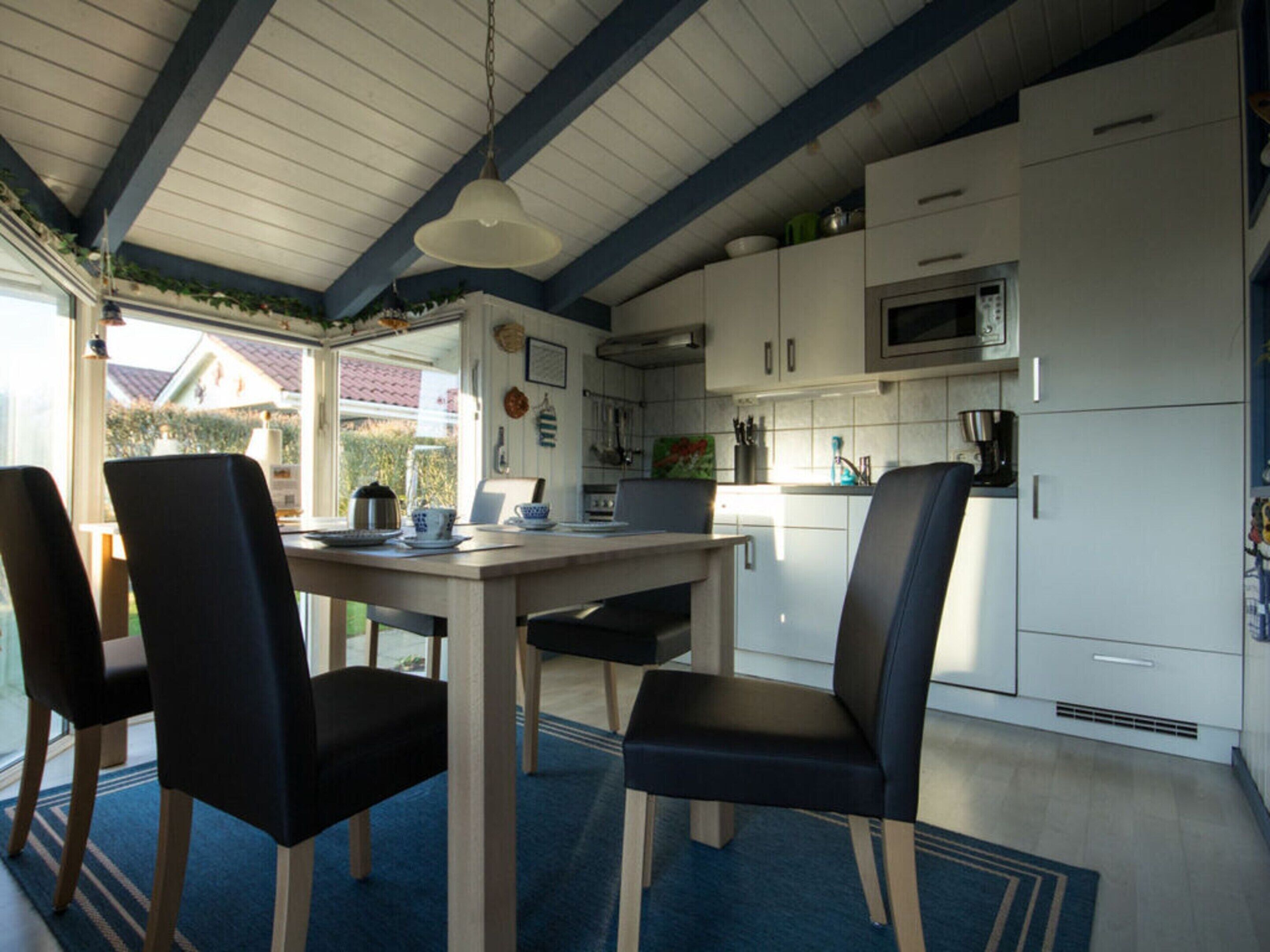 Een moderne keuken met witte kasten, een magnetron, en een eethoek met een tafel en stoelen.