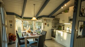 A modern kitchen with white cabinets, a built-in oven, and a dining area with a table and chairs. - Holiday House Solvej (Brodersby)