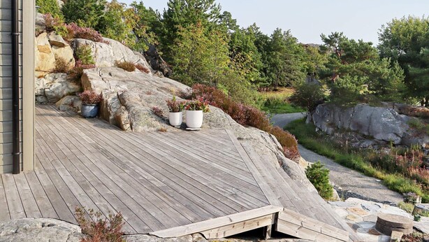 A wooden deck with potted plants, a stone wall, and a rocky landscape with trees.