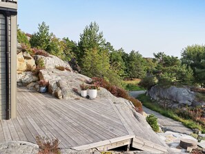 A wooden deck with potted plants, a stone wall, and a rocky landscape with trees.