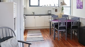 A compact kitchen with a window, a dining table with chairs, and a refrigerator.