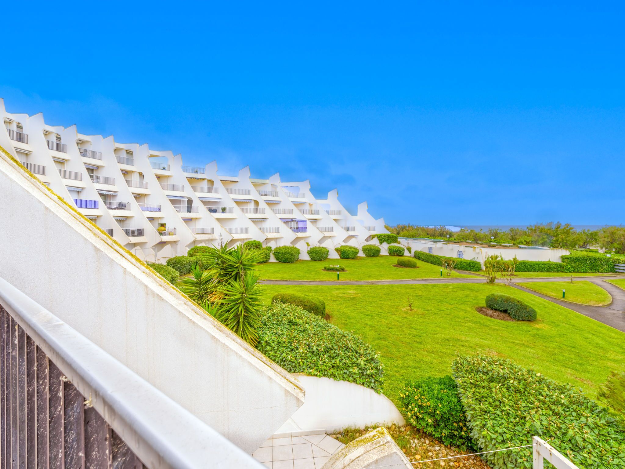 A modern hotel with a unique zigzag architectural design, featuring balconies and a well-maintained lawn.