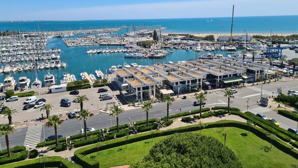 A marina with numerous boats docked, a parking area, and a road with palm trees. - Le Parador by Interhome (La Grande Motte)