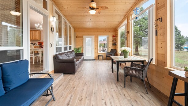 Una habitación acogedora con techo de madera, un sofá azul, una mesa de comedor con sillas y ventanas amplias que ofrecen vistas al exterior.