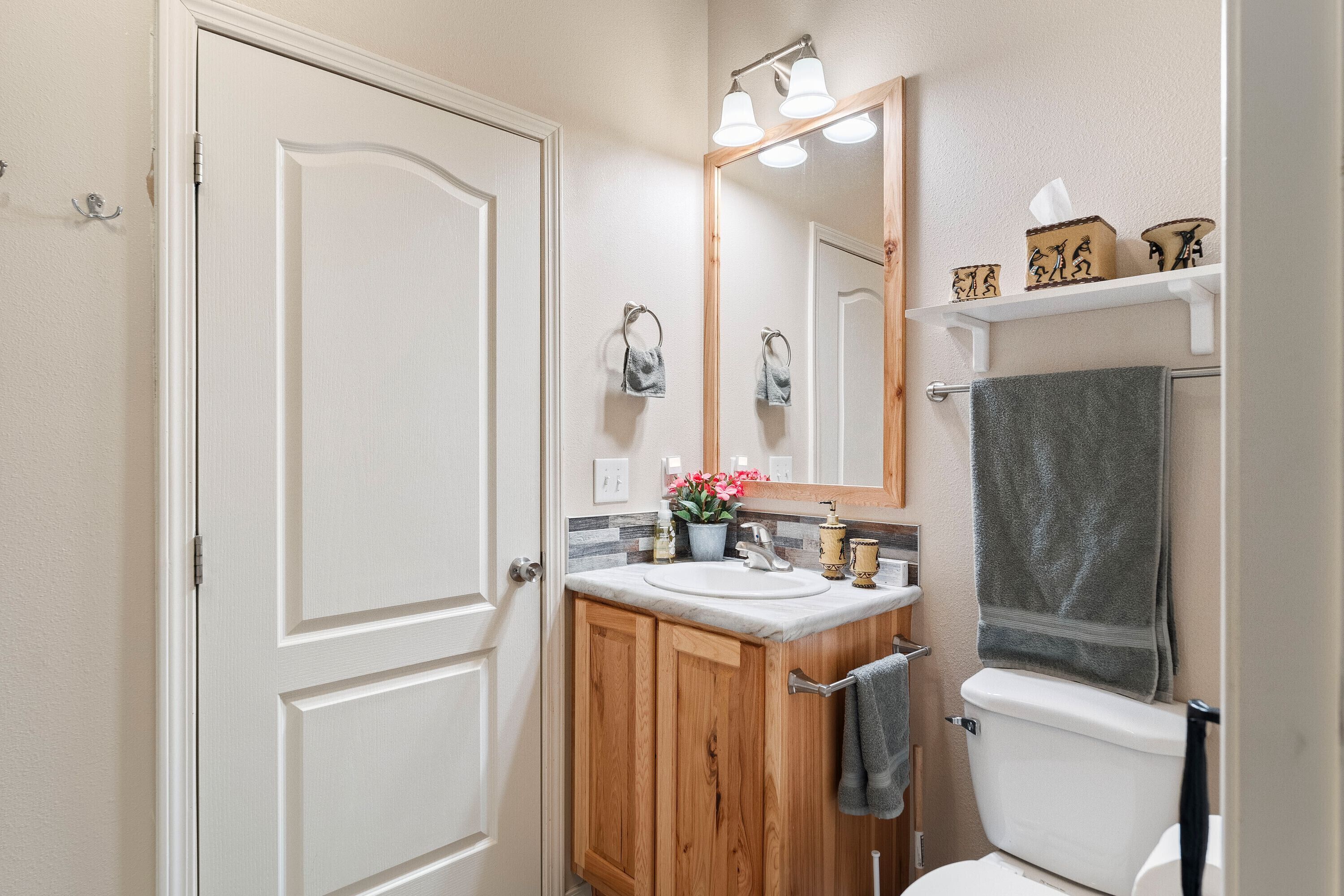 A bathroom with a white door, wooden cabinets, a sink, a mirror, and a toilet.
