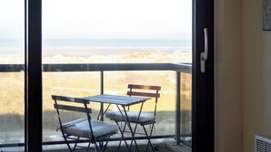 Een balkon met een tafel en twee stoelen, uitkijkend op een strand.