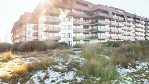 Een meerlaags woongebouw met balkons, omringd door besneeuwde grond en gras.