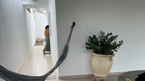 A hallway with a hammock, a potted plant, and a round table with stools.
