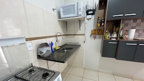 A kitchen with a gas stove, a microwave, and a sink. There are cabinets and a countertop with various items on it.