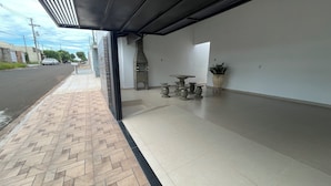 A covered outdoor area with a herringbone-patterned walkway, a stone grill, and a potted plant.