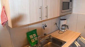 Eine Küche mit hellen Holzschränken, einer Edelstahlspüle, einer Mikrowelle und einer Kaffeemaschine.