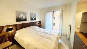 A hotel room with a large bed, a wooden headboard, a small desk, and two wall-mounted artworks. - Apartment in Nieuwpoort Near the Beach (Nieuwpoort)