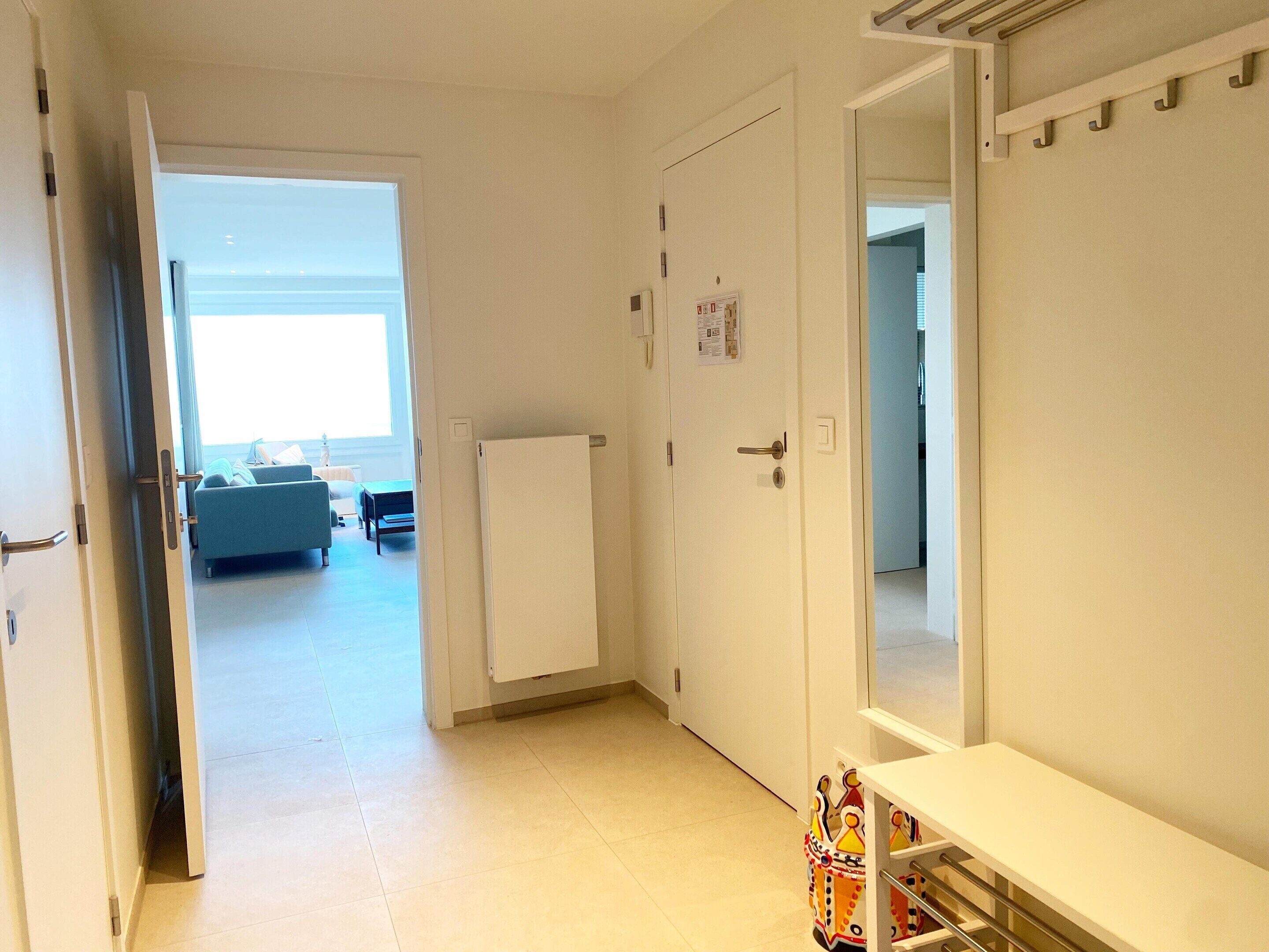 En gang med en hvid dør, en radiator og et lille bord med en farverig genstand på.