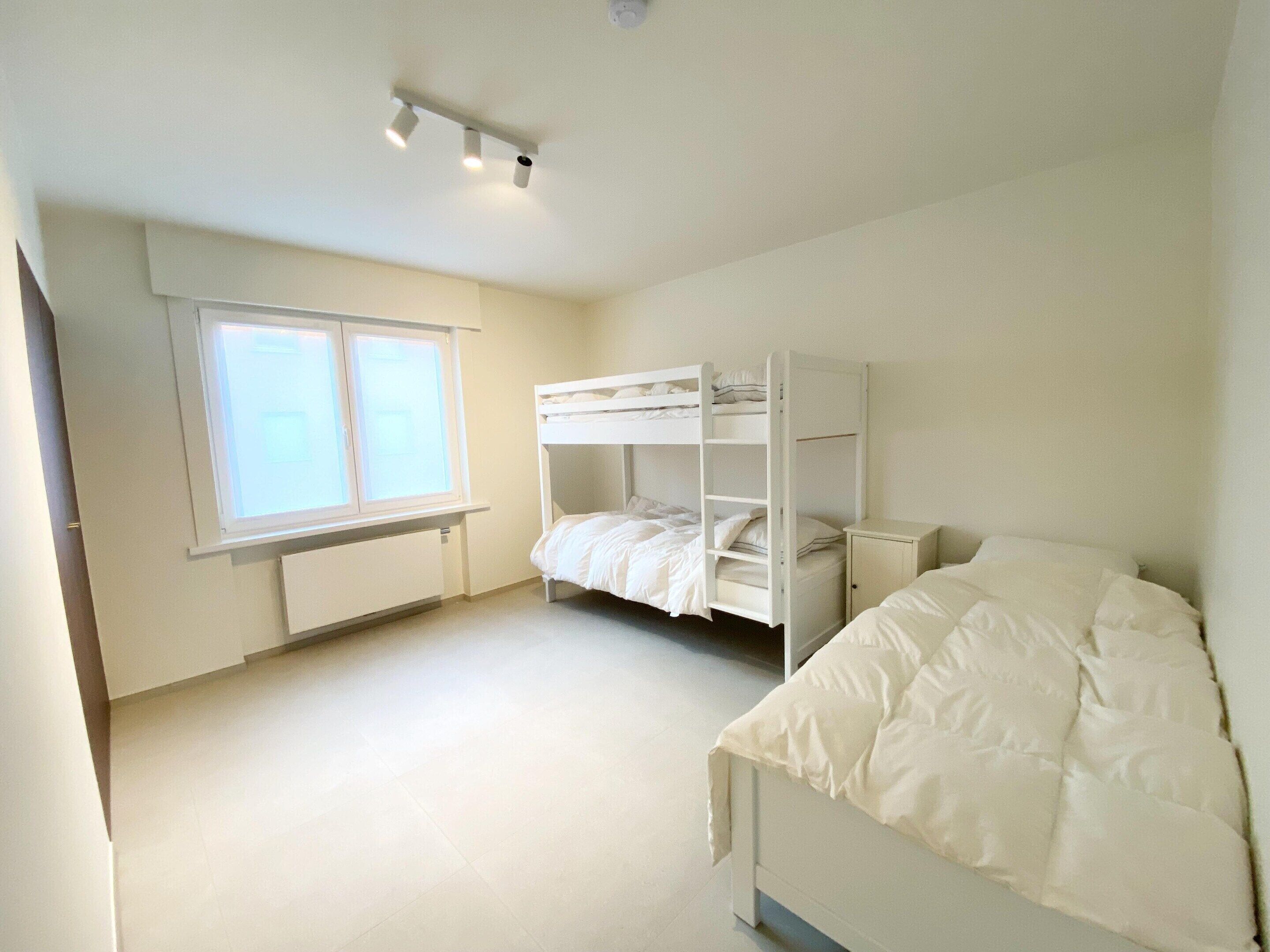 A bedroom with a bunk bed, a single bed, a window, and a radiator.