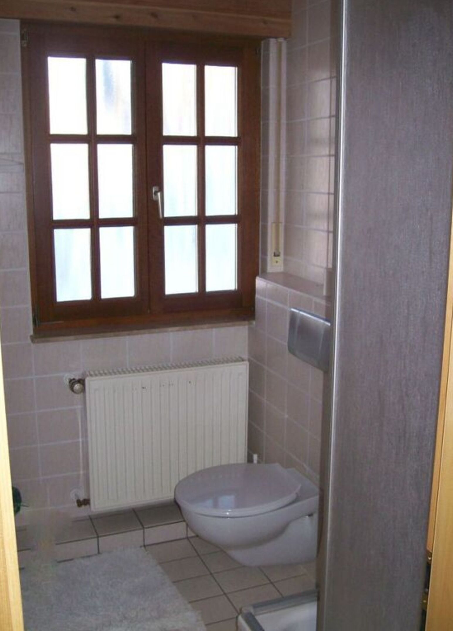 A small bathroom with a toilet, a window, and a radiator.