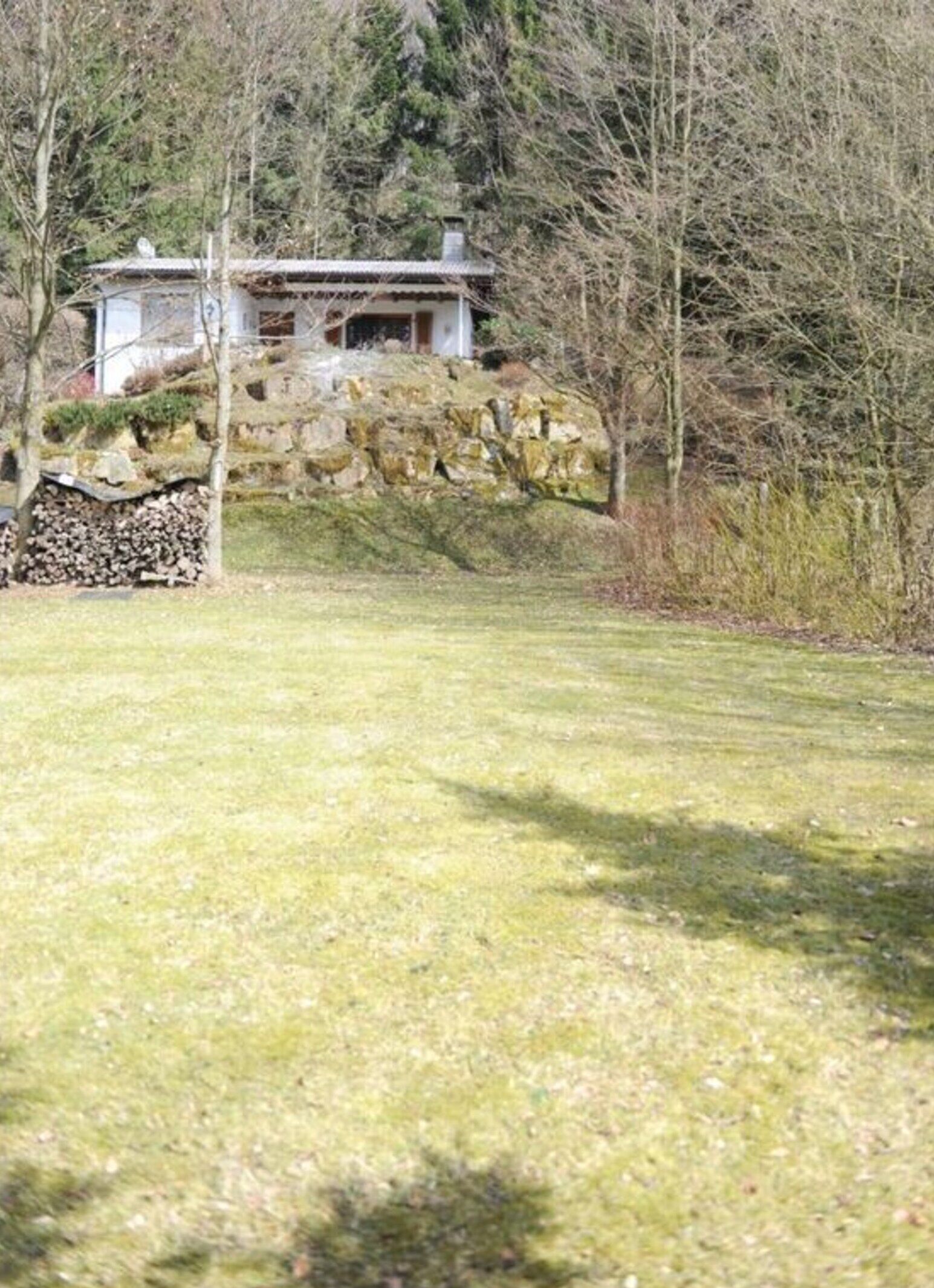 A rustic cabin with a stone foundation, surrounded by a grassy field and trees.