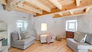 Ein Loft-Zimmer mit freiliegenden Holzbalken, zwei grauen Sofas, einem weißen Sofa und einer kleinen Holzkommode.