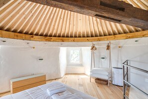 A room with a sloped wooden ceiling, a bed with white linens, a wooden dresser, a small window, and a white heater. - Ericeira Windmill by Hopstays | Wild Refuge (Mafra)