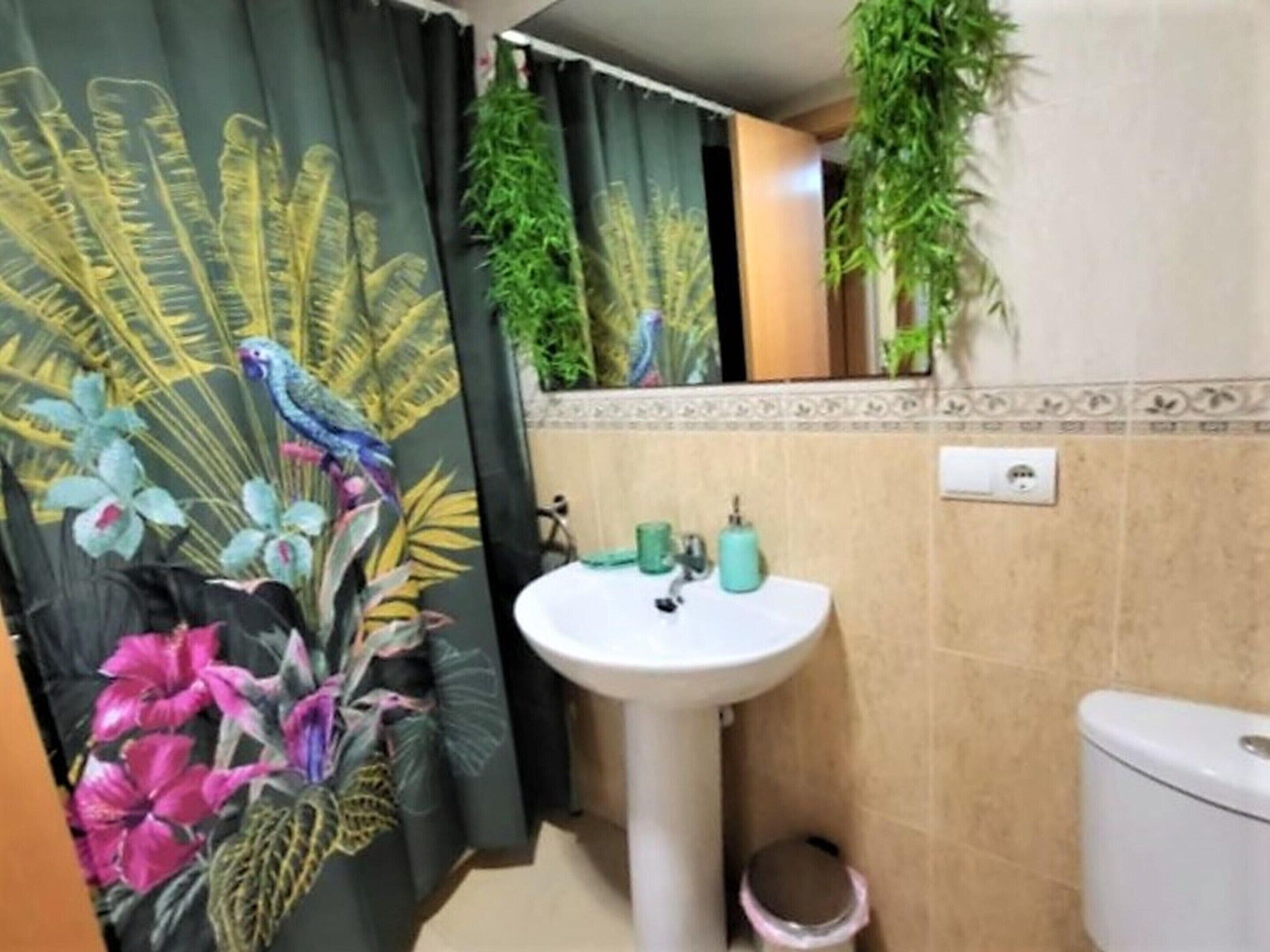 A bathroom with a white sink, a toilet, and a shower curtain with a tropical design.