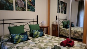 A hotel room with a bed, green pillows, a nightstand, a mirror, and tropical-themed artwork on the wall. - Villa in Spain With Private Pool (Vera)