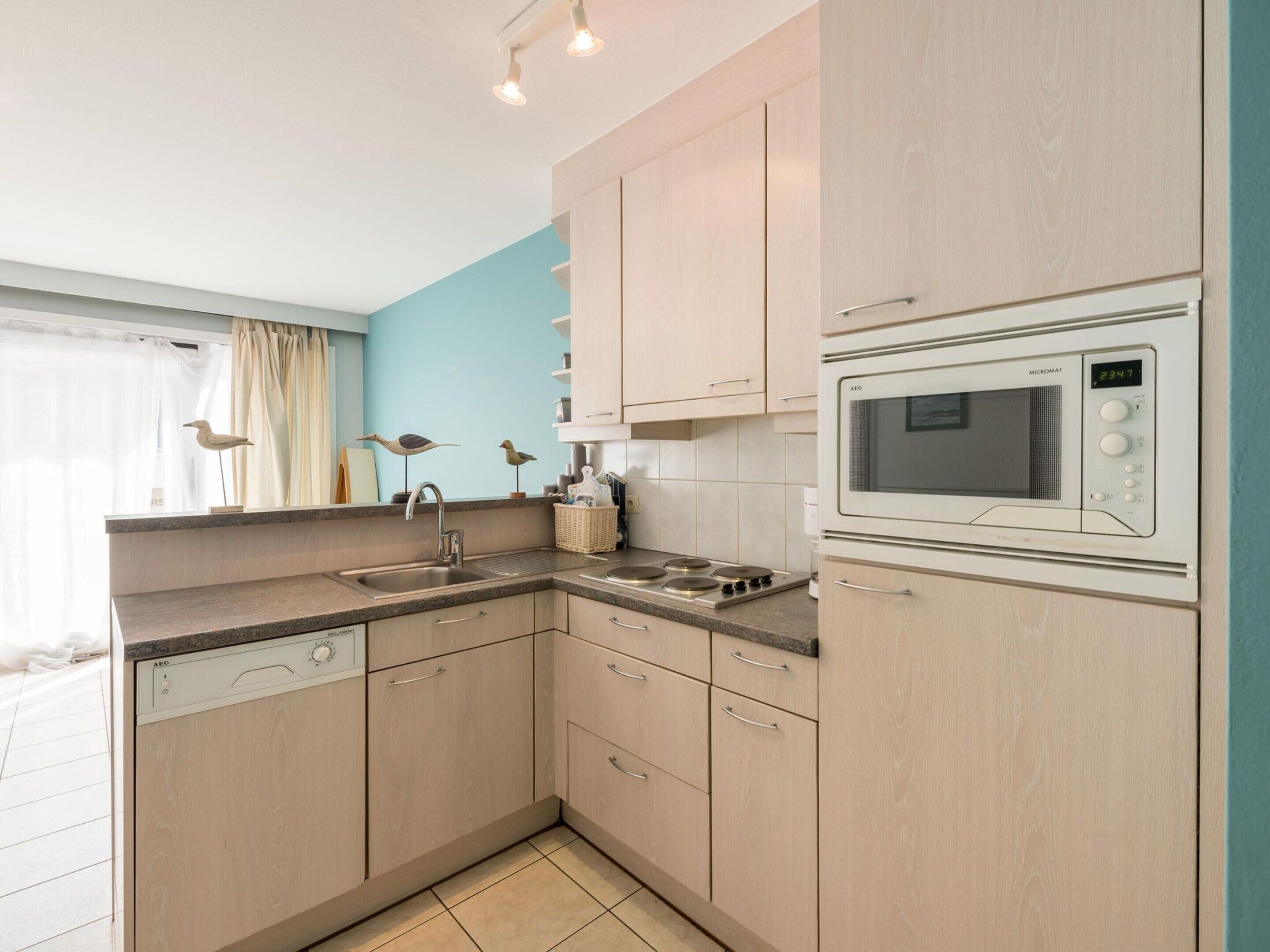 A modern kitchen with light wood cabinets, a built-in dishwasher, a microwave, and a gas stove.