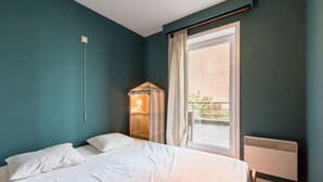 Une chambre à coucher avec un lit, une table de chevet, une lampe, une fenêtre avec des rideaux et une vue sur l’extérieur.