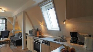 A compact kitchen with a built-in oven, microwave, and dishwasher, a dining area with a table and chairs, and a large skylight providing natural light. - Villa Balticum Modern Retreat (Zingst)