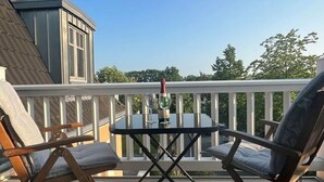 A balcony with two wooden chairs and a small table, a glass of wine, and a view of trees and a building. - Villa Balticum Modern Retreat (Zingst)