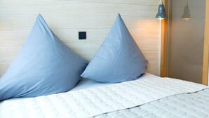 Ein Bett mit zwei Kissen und einer weißen Decke, ein Holzkopfende und eine Wandleuchte.