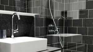 Ein modernes Badezimmer mit einem weißen Waschbecken, einer Handbrause und einer Duschkabine aus Glas.