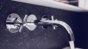 Ein modernes Badezimmer mit einem chromfarbenen Wasserhahn und einer Wand aus dunklem Marmor.